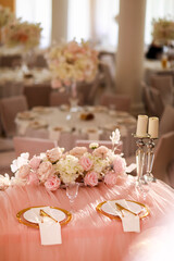 table decoration with pink tablecloth, crystal candlesticks with candles and white pink flowers in restaurant . stylish wedding day. setting table with gold plate, fork and knife