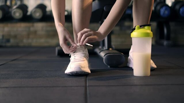 4k slow motion, Active woman tying shoelaces on sports shoes. Female athlete legs in sneakers and hands tying shoelaces in fitness gym.