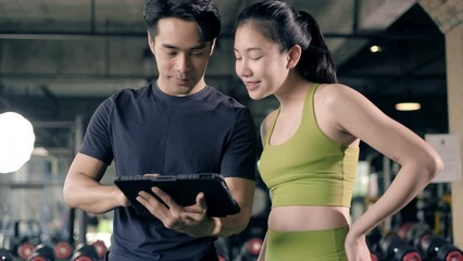 4k resolution, Personal coach trainer looking at digital tablet and explaining progress to young woman at the fitness gym. Workout training in fitness gym.