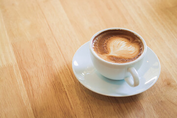 Heart shaped hot coffee latte in a white mug placed on a wooden floor. Copy space
