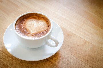 Heart shaped hot coffee latte in a white mug placed on a wooden floor. Copy space
