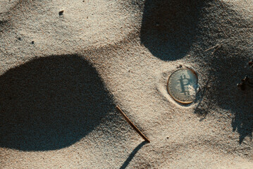 A bitcoin coin lies in the sand on the beach. The concept of payment for nature. Copy space.
