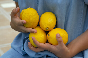 girl in a denim sundress holding yellow lemons in her hands,
