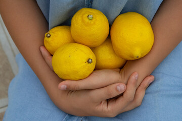 children's hands hold lemons, yellow lemon blue denim sundress