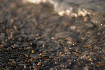 A transparent sea wave rolls over a rocky beach, the concept of rest and travel, calmness and reflection on a warm summer day, defocusing, blurred background, selective focus, bokeh.