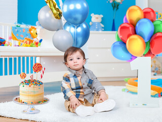 child with birthday cake . A one year old baby sitting on his fur next to a birthday cake and balloons