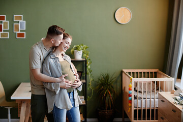 Young man kissing and caring about his pregnant wife while they standing in the room