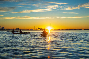 Sea kayakers paddling across Toronto's Inner Harbour just as the rising sun breaks the horizon.  Shot in summer.  Room for text.