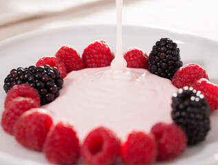 fresh raspberries and blackberries laid out on a white plate in circle with yogurt