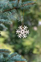 Wooden handmade snowflake hangs on the branch of Blue Spruce tree. Christmas or New Year greeting concept. Free copy space