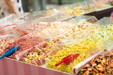 colorful candy, jelly sweets in plastic boxes on showcase in sweet-shop, matured woman is on background. Smart healthy lifestyle, snacks. Horizontal plane