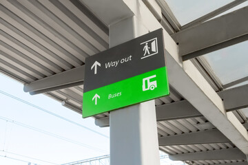 Sign green showing where the exit way out and stop of public transport buses are located under the roof of the railway platform.