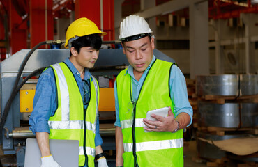 Two Asian male engineers use a tablet to discuss production plans and inspect production machines.