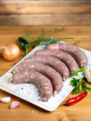 Turkey raw meat sausages with vegetables on plate on wooden background. 