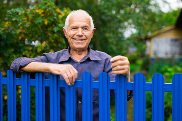 Portrait of pensive elderly man at fence of his country house in village