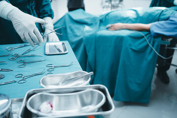 Fototapeta premium Close up surgeon doctor's hand with hygiene glove taking sterile surgical instrument tool, equipment in operating room patient in background for surgery. Hospital, medical healthcare emergency concept