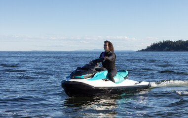 Adventurous Caucasian Woman on Water Scooter riding in the Ocean. Howe Sound and mountain landscape in background. West Vancouver, British Columbia, Canada.