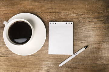 Obraz na płótnie Canvas Coffee in a white cup on a wooden table. Notepad with space for text