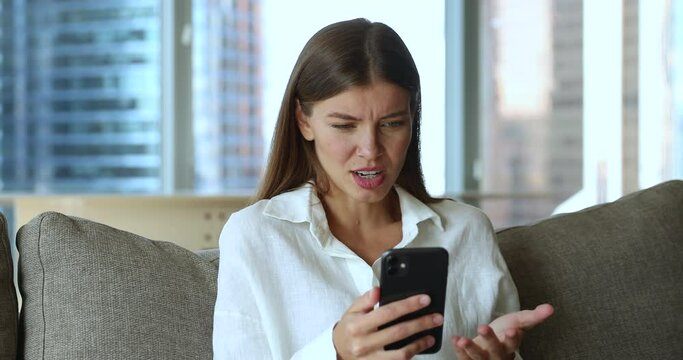 Young woman sit on sofa at home using cellphone read bad news in message looks upset, feels angry due to smartphone mobile app crash, wi-fi connection problem, get spam messages, broken gadget concept