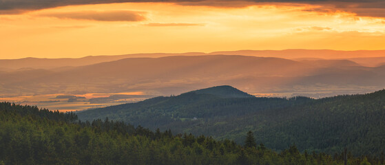 Poland, the Sudetes, mountain landscape in the Snieznik massif, mountain peaks and a valley illuminated by the rays of the setting sun.