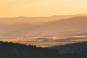 Poland, the Sudetes, mountain landscape in the Snieznik massif, mountain peaks and a valley illuminated by the rays of the setting sun.