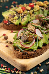 An avocado toast with mushrooms, radish, sesame seeds and chive on a wooden cutting board.