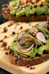 An avocado toast with mushrooms, radish, sesame seeds and chive on a wooden cutting board.