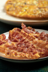 Close up of some crispy bacon slices and three fresh eggs on the background.