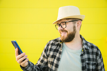 Portrait of attractive cheerful guy using smartphone for scrolling on social media over bright...