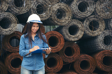 Asian woman engineer fill out form or inspect at construction site. Civil Engineer writing, and checklist at building project with roll of wire mesh background. Engineer and worker inspect concept.