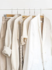 Woman's linen and cotton wardrobe in shades of beige on white. Rack with neutral female clothes on...