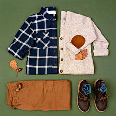 Autumn boy outfit on green background. Little Boy's Autumn Fashion. Kids sweater, shirt, pants and boots arranged with acorns and oak leaves. Autumn or Thanksgiving day mood. Flat lay, top view.