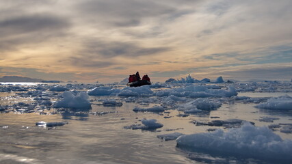 Zodiac inflatable boat navigating among icebergs at sunset, in Cierva Cove, Antarctica