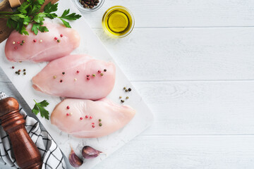 Chicken breast. Two Chicken fillet with spices, olive oil and parsley on white stone cutting board on white wooden table background. Top view with copy space. Food meat cooking background.
