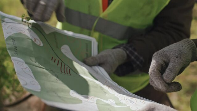 Close-up of two cropped foresters holding map of area, standing in forest on sunny spring day, talking