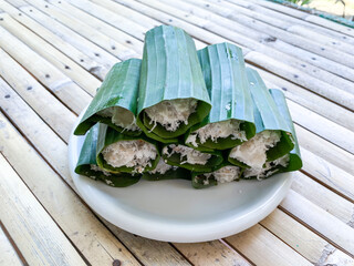 A traditional Putu snack from Indonesia, made of glutinous rice, steamed on a bamboo tube and grated coconut as topping then covered with banana leaf.