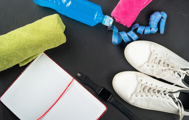 Fitness concept. Towel, sneakers, a bottle of isotonic drink, notepad, smart watch, measuring tape on a dark concrete background, top view. copy space