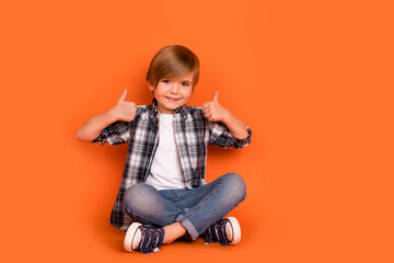 Full length photo of young boy sit floor show thumbs-up feedback select good isolated over orange color background
