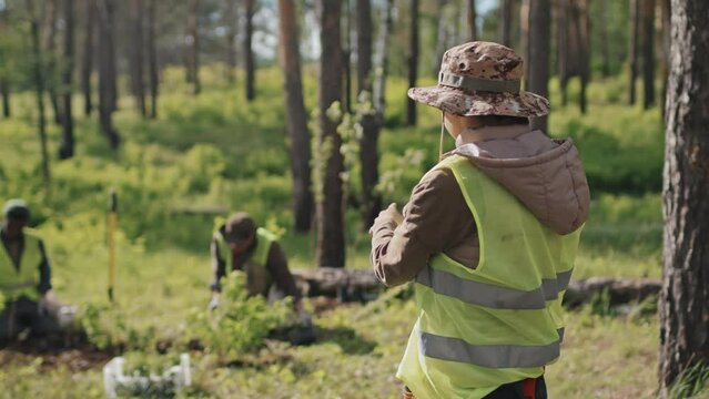 Medium of young Asian female forester talking on mobile phone, standing in forest on sunny summer day