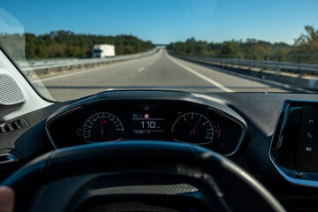 Driver view to the speedometer at110 kmh or 110 mph and the road blurred in motion, day light view...
