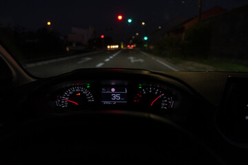 Driver view to the speedometer at 35 kmh or 35 mph, on road with traffic lights blurred in motion,...