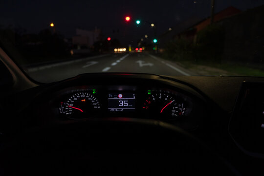 Driver view to the speedometer at 35 kmh or 35 mph, on road with traffic lights blurred in motion, night fall view from inside a car of driver POV of the road landscape.