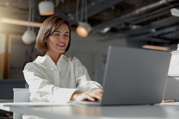 Fototapeta premium Smiling european business woman working laptop while sitting in cozy cafe. Blurred background