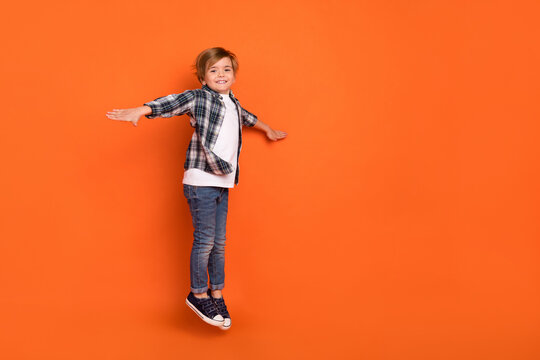 Full body profile side photo of young excited boy jumper arms wings fly isolated over orange color background