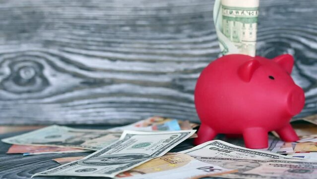 Piggy bank among dollar and euro banknotes. Money sticks out of her. Difficulties in saving money. Multicurrency savings.