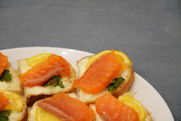Red salmon fish sandwiches with lemon wedges on a piece of bread.