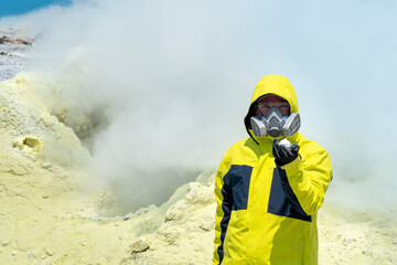 man volcanologist on the background of a smoking fumarole demonstrates a sample of a mineral
