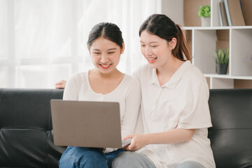Obraz na płótnie Canvas Asian woman happy holding laptop phone sitting sofa smiling good mood indoors indoors
