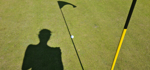 Shadow of golfer near flag on green green