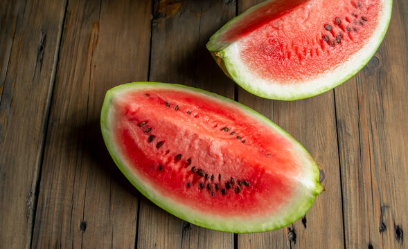 Two slices of sweet, red watermelon on a brown tree. Watermelon quarters on a wooden table.